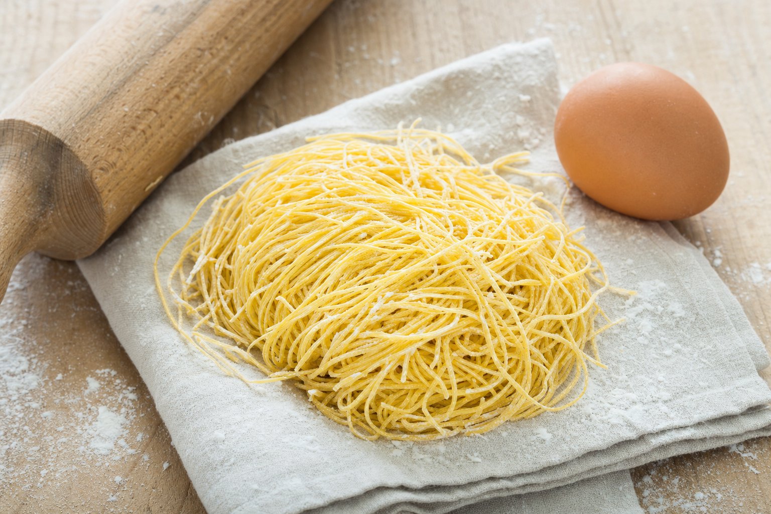 Nido di fieno di Canepina giallo paglierino su canovaccio chiaro, con uovo e farina sparsa su tavolo di legno naturale.